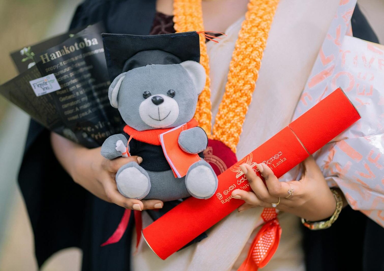 Close-up of a graduate holding a cute teddy bear and diploma at a ceremony.